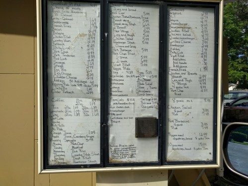 Menu board displaying various food items and prices, including sandwiches, salads, and sides.
