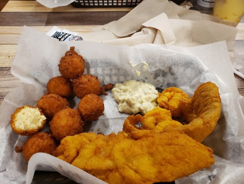 A basket of fried fish, hushpuppies, and a side of tartar sauce on a paper-lined tray.