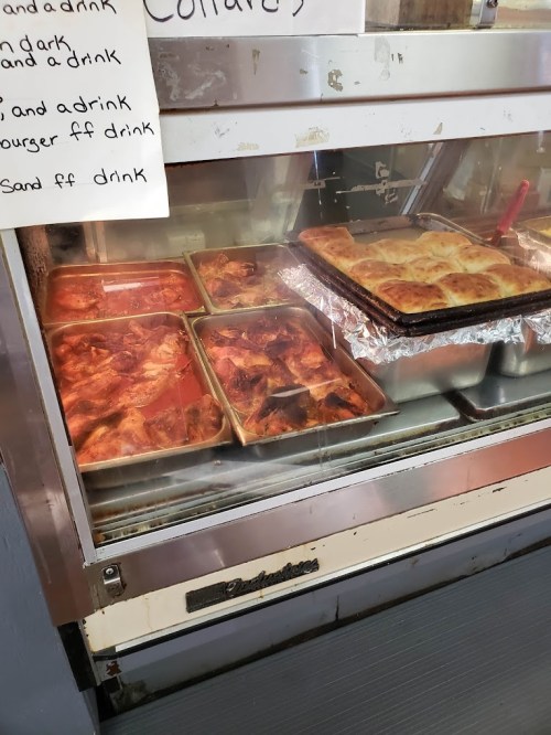 A display case with trays of baked dishes, including chicken and a casserole, behind a glass front.