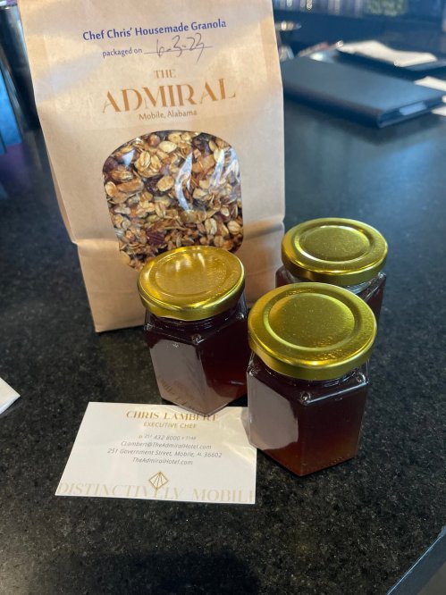 A bag of granola labeled "The Admiral" next to three small jars of honey and a business card for Chef Chris Lambert.
