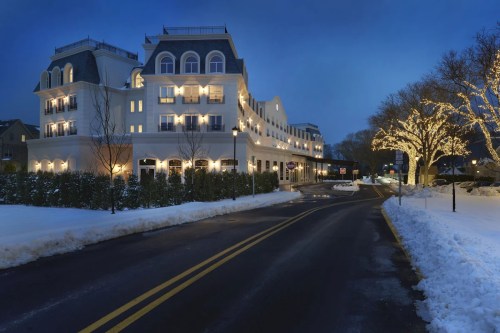 A charming hotel illuminated at night, surrounded by snow and festive lights along the road.