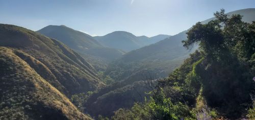 A scenic view of rolling hills and mountains under a clear blue sky, with lush greenery in the valley below.