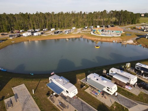 Aerial view of a campground with RVs around a pond, surrounded by trees and a recreational area.