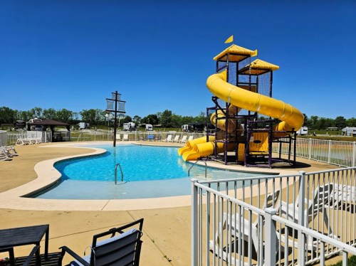 A sunny pool area featuring a water slide, lounge chairs, and a fenced-in swimming pool.