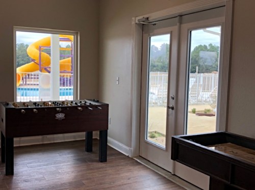 A room with a foosball table and large windows overlooking a pool area with a water slide.