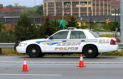 Akron police car parked on the roadside with traffic cones nearby and a cityscape in the background.