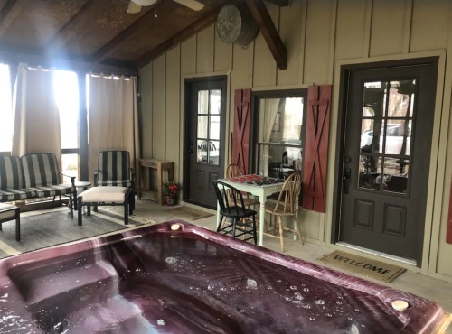 A cozy indoor space featuring a hot tub, seating area, and doors leading outside, with a "WELCOME" mat at the entrance.