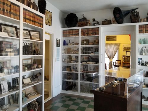A museum display featuring shelves of historical artifacts, photographs, and vintage items in a well-lit room.