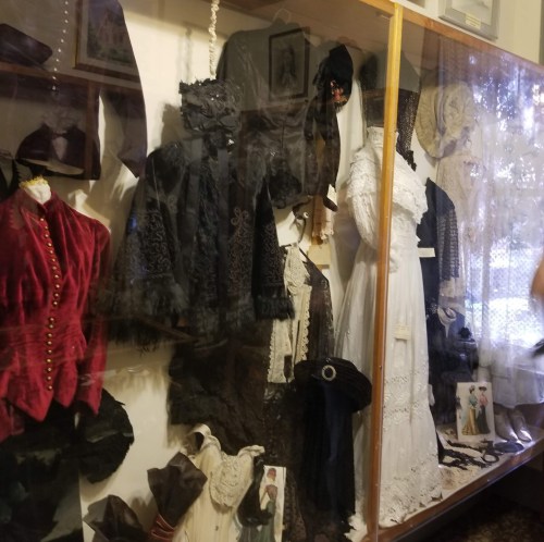 Display case featuring vintage clothing, including dresses and jackets, showcasing intricate designs and historical styles.