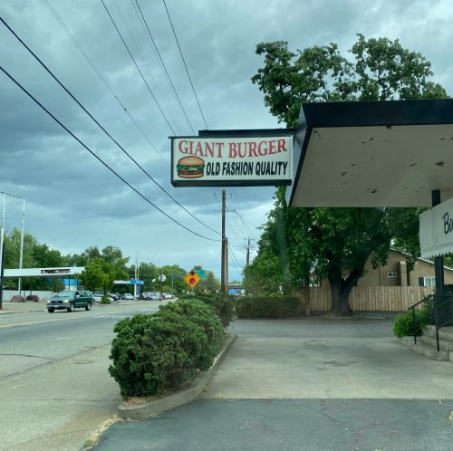 Sign for "Giant Burger" with the tagline "Old Fashion Quality," set against a cloudy sky and roadside view.