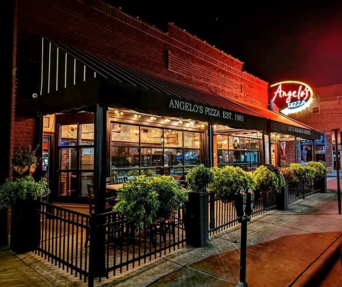 A cozy pizza restaurant at night, featuring outdoor seating and warm lighting, with a sign reading "Angelo's Pizza."
