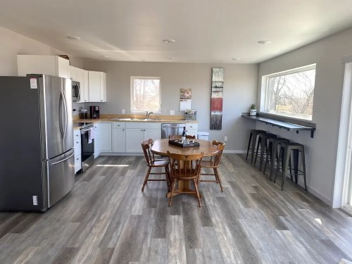 Bright, modern kitchen with stainless steel appliances, a wooden dining table, and bar stools by the window.