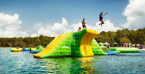 A colorful inflatable water park with people jumping and playing on a sunny day by the lake.