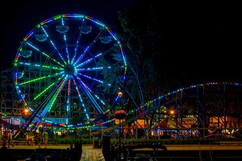 A brightly lit Ferris wheel and roller coaster at night, surrounded by colorful lights and a festive atmosphere.