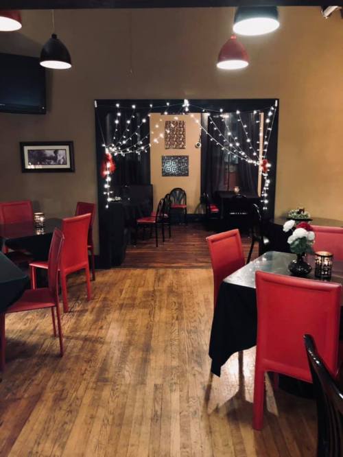Cozy restaurant interior with red chairs, black tables, and string lights creating a warm ambiance.