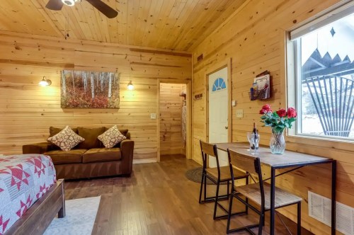 Cozy wooden interior with a sofa, dining table, and decorative flowers, featuring warm lighting and natural textures.
