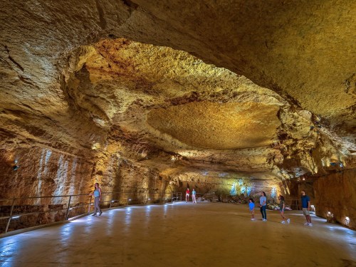 A spacious underground cave with illuminated rock formations and visitors exploring the area.
