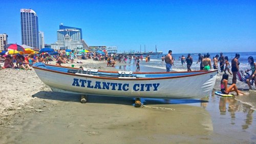 A beach scene in Atlantic City with a boat on the sand, colorful umbrellas, and people enjoying the sun and water.