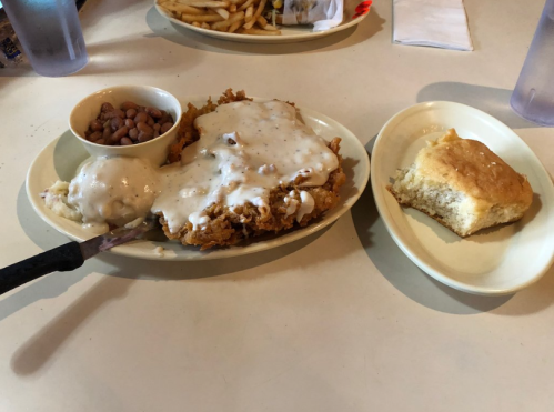 A plate of fried chicken smothered in gravy, served with mashed potatoes, pinto beans, and a piece of cornbread.