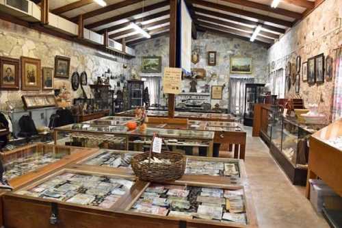 Interior of a museum featuring display cases with artifacts, vintage items, and historical photographs on stone walls.