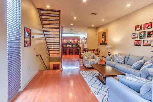 A modern living room with a staircase, featuring a blue sofa, wooden floors, and framed photos on the walls.