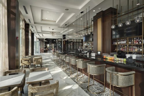 Elegant bar area with high stools, marble floors, and stylish decor, featuring a well-stocked bar and large windows.