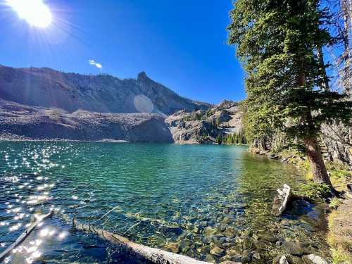 A serene lake surrounded by rocky mountains and trees, with sunlight reflecting on the water's surface.