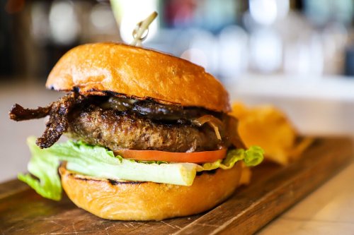 A juicy burger with lettuce, tomato, and crispy bacon on a toasted bun, served with a side of chips on a wooden board.