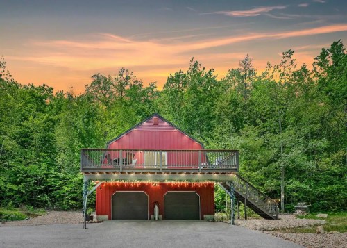 A red barn-style building with a deck, surrounded by trees, under a colorful sunset sky.
