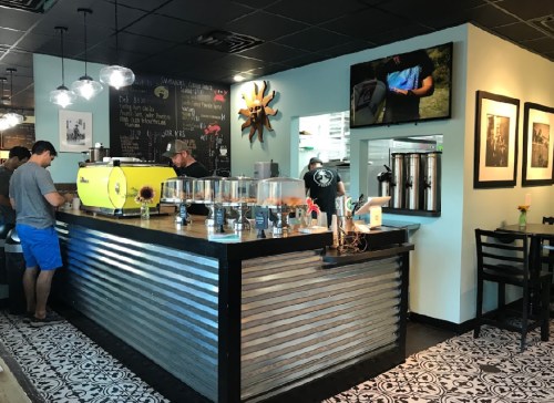 A cozy café interior with a metal counter, coffee machines, and patrons enjoying drinks in a stylish setting.