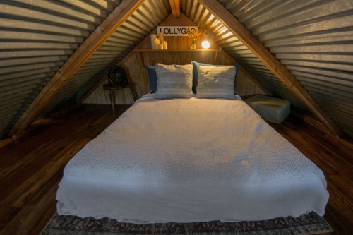 Cozy attic bedroom with a bed, decorative pillows, and warm lighting under a sloped, corrugated metal ceiling.