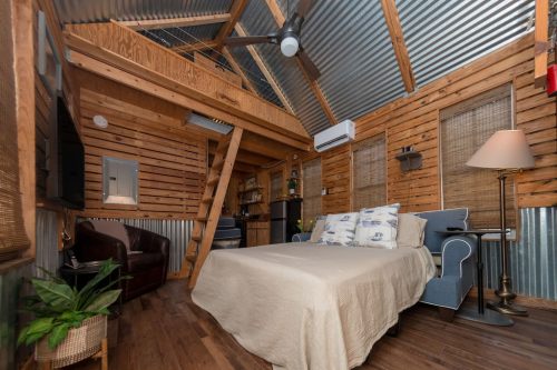 Cozy interior of a rustic cabin featuring a bed, seating area, wooden beams, and metal accents.