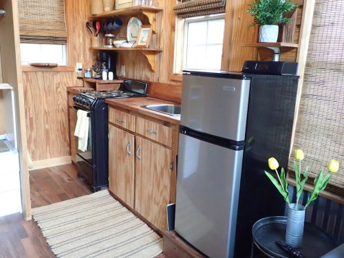 Cozy kitchen with wooden cabinets, a stove, sink, fridge, and a vase of yellow tulips on a table.