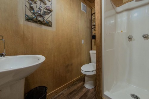 A small bathroom featuring a shower, toilet, sink, and wooden walls with a fish-themed wall decoration.