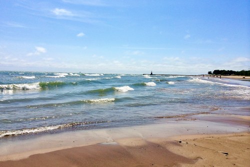 A serene beach scene with gentle waves, sandy shore, and a clear blue sky in the background.