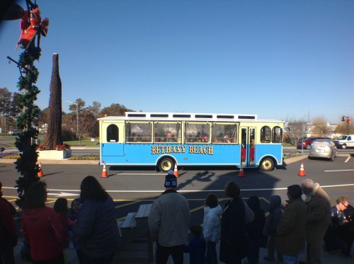 A blue and yellow trolley labeled "BETHANY BEACH" drives past a crowd of people on a sunny day.