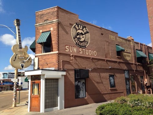 Exterior of Sun Studio, featuring a large guitar sign, brick walls, and a clear blue sky.