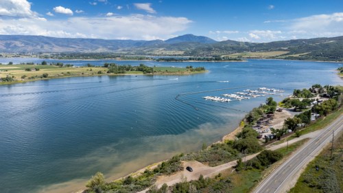 Aerial view of a serene lake surrounded by greenery and mountains, with a marina and road along the shore.