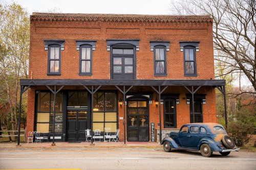 Historic brick bank building with large windows, a welcoming sign, and a vintage car parked outside.