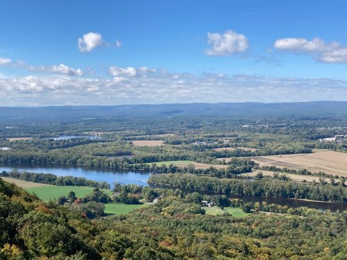 A scenic view of a river winding through green fields and hills under a blue sky with scattered clouds.