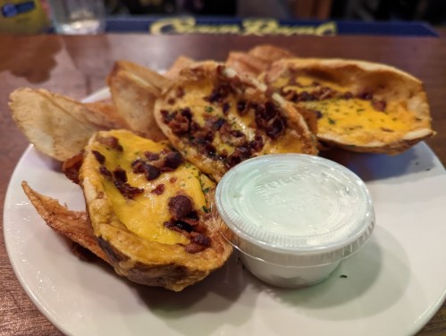 A plate of potato skins topped with cheese and bacon, served with a side of ranch dressing.
