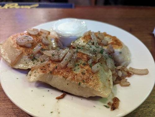 A plate of golden-brown pierogi topped with sautéed onions and served with a side of sour cream.