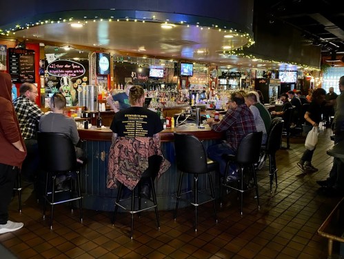 A lively bar scene with patrons seated at the counter, drinks in hand, and a warm, inviting atmosphere.