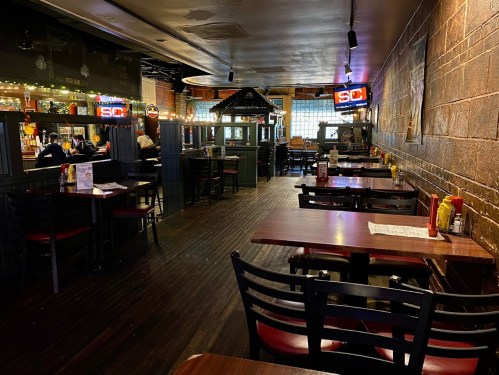 Interior of a restaurant with empty tables, wooden floors, and neon signs, creating a cozy atmosphere.