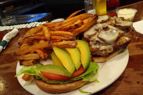 A plate featuring a burger topped with mushrooms and cheese, alongside crispy fries and a side of lettuce and tomato.