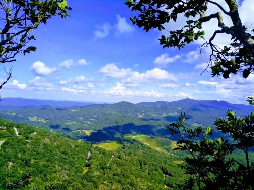 A panoramic view of lush green mountains under a bright blue sky with scattered clouds.