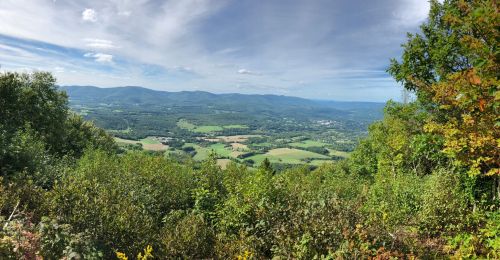 A panoramic view of rolling green hills and valleys under a blue sky with scattered clouds.