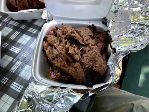 A takeout container filled with tender, sliced brisket resting on a foil-lined surface.