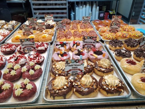 A display of colorful donuts with various toppings and flavors, each labeled with a name on small signs.
