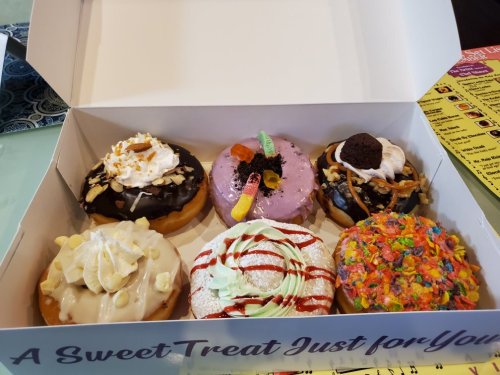 A box of six colorful donuts with various toppings, including sprinkles, frosting, and candy.